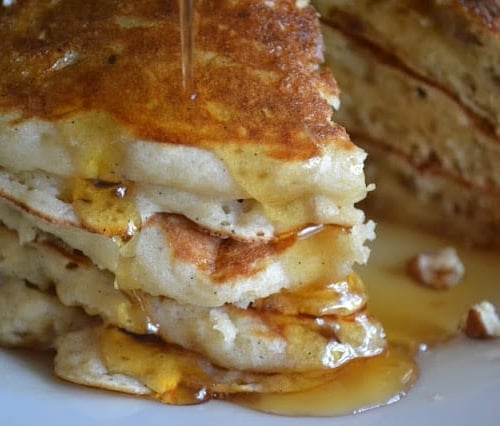 A stack of banana buttermilk pancakes with dripping syrup