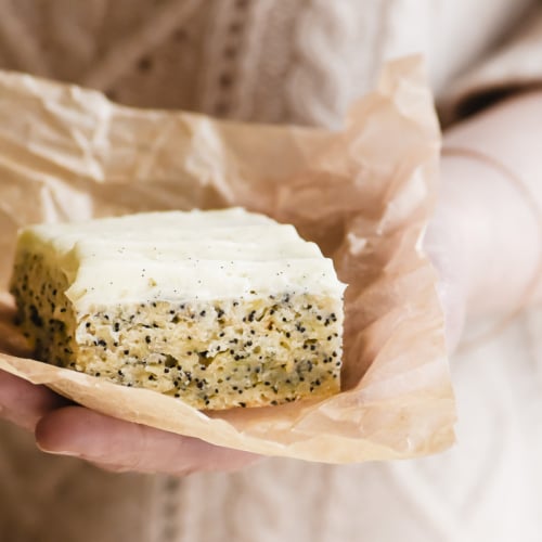 Holding a slice of banana snack cake with vanilla bean frosting, on parchment paper.