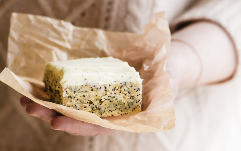 Holding a slice of banana snack cake with vanilla bean frosting, on parchment paper.