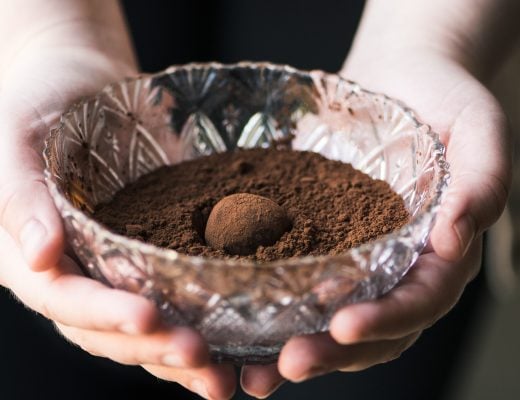 hands holding a glass bowl with cocoa powder and a chocolate truffle