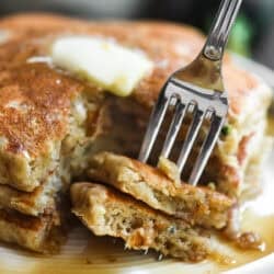 Taking a bite of a stack of zucchini bread pancakes with butter and maple syrup.