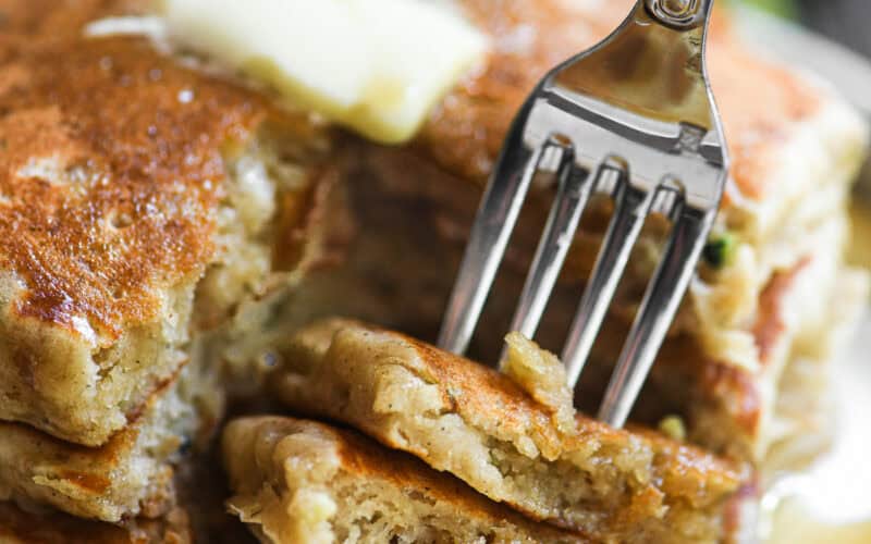 Taking a bite of a stack of zucchini bread pancakes with butter and maple syrup.