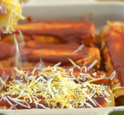 Sprinkling grated cheese on cheese and onion enchiladas.