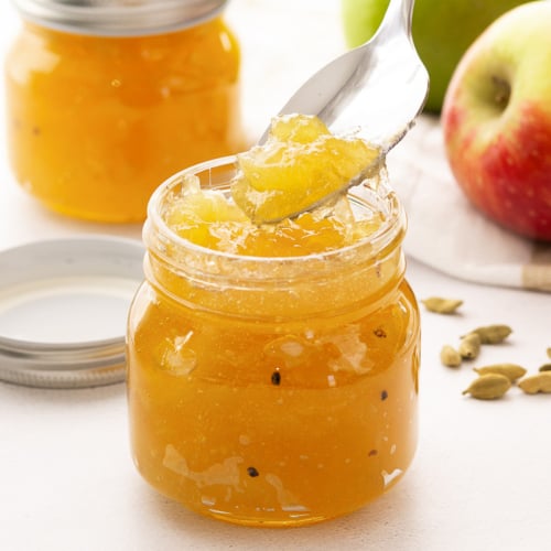 Golden French apple jam in a small jar with spoon.