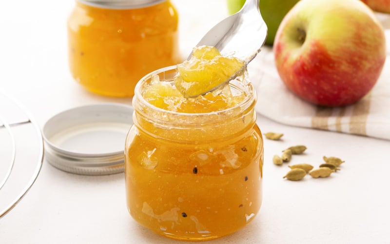 Golden French apple jam in a small jar with spoon.
