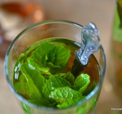 Photo of a glass of Sweet Moroccan Mint Tea with mint leaves and a spoon.