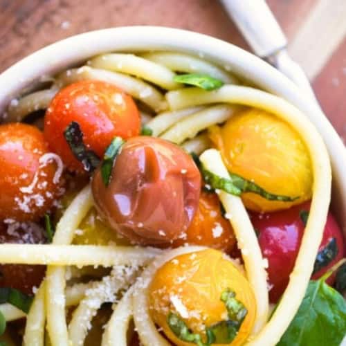 overhead view of a small bowl with bucatini and burst tomatoes.
