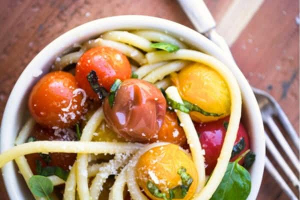 overhead view of a small bowl with bucatini and burst tomatoes.