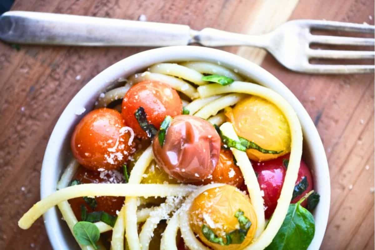 bucatini with burst tomatoes in a white pasta bowl.