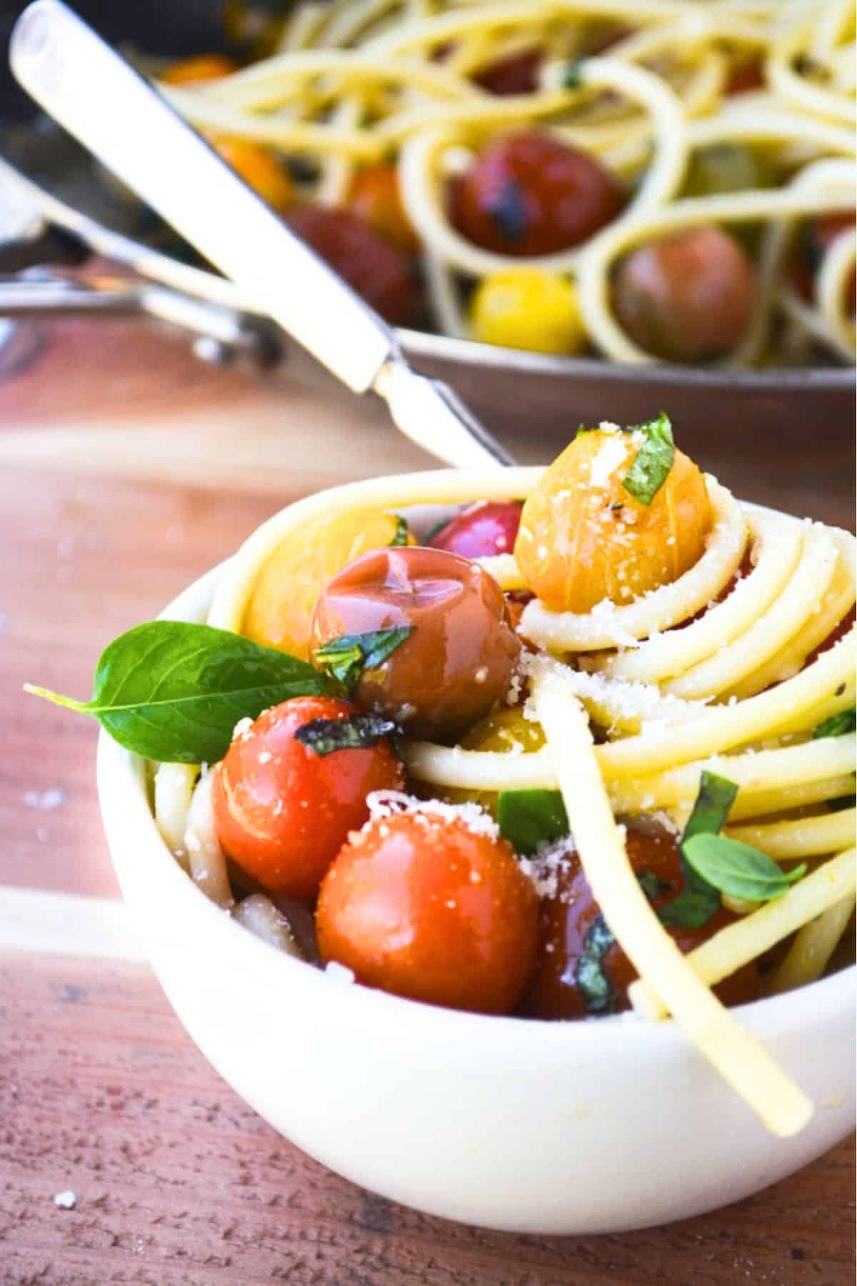 Bucatini with Burst Tomatoes is a gloriously healthy pasta recipe made with juicy, colorful cherry tomatoes and fresh basil ~ no matter what the calendar says, this recipe screams summer! #easy #recipe #bucatini #pastarecipe #tomatoes #cherrytomatoes #summerpastarecipe #healthypastarecipe #vegetarianpasta #vegetarian #dinner #30minutemeal #vegan #vegetarian #heirloomtomatoes bucatini with burst tomatoes in a small white bowl.