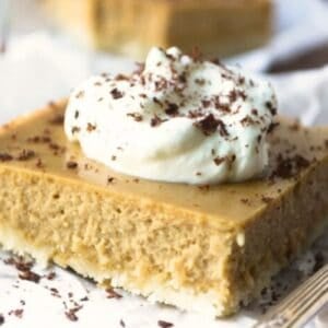 An Irish Cream Cheesecake bar with whipped cream on parchment paper.
