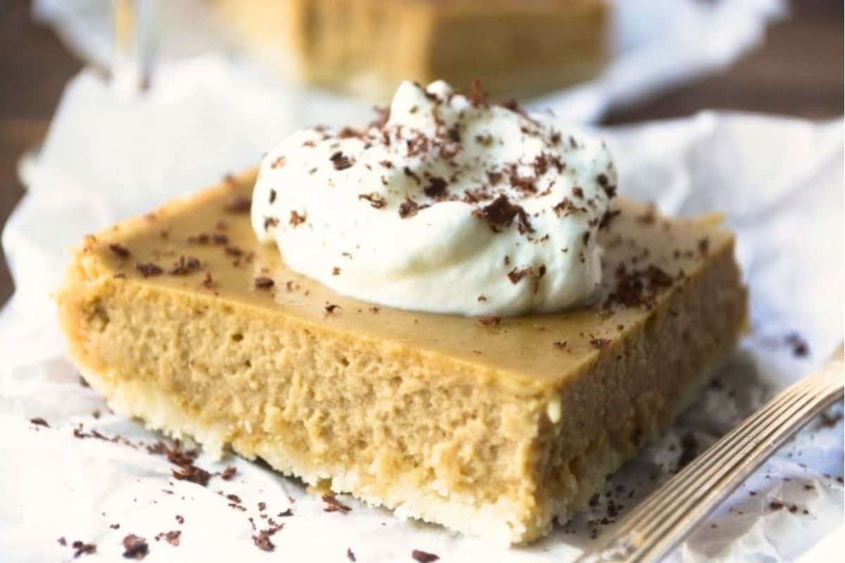 An Irish Cream Cheesecake bar with whipped cream on parchment paper.