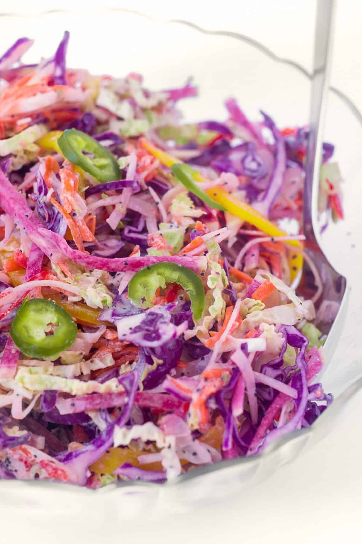 Rainbow slaw in a bowl with salad servers.