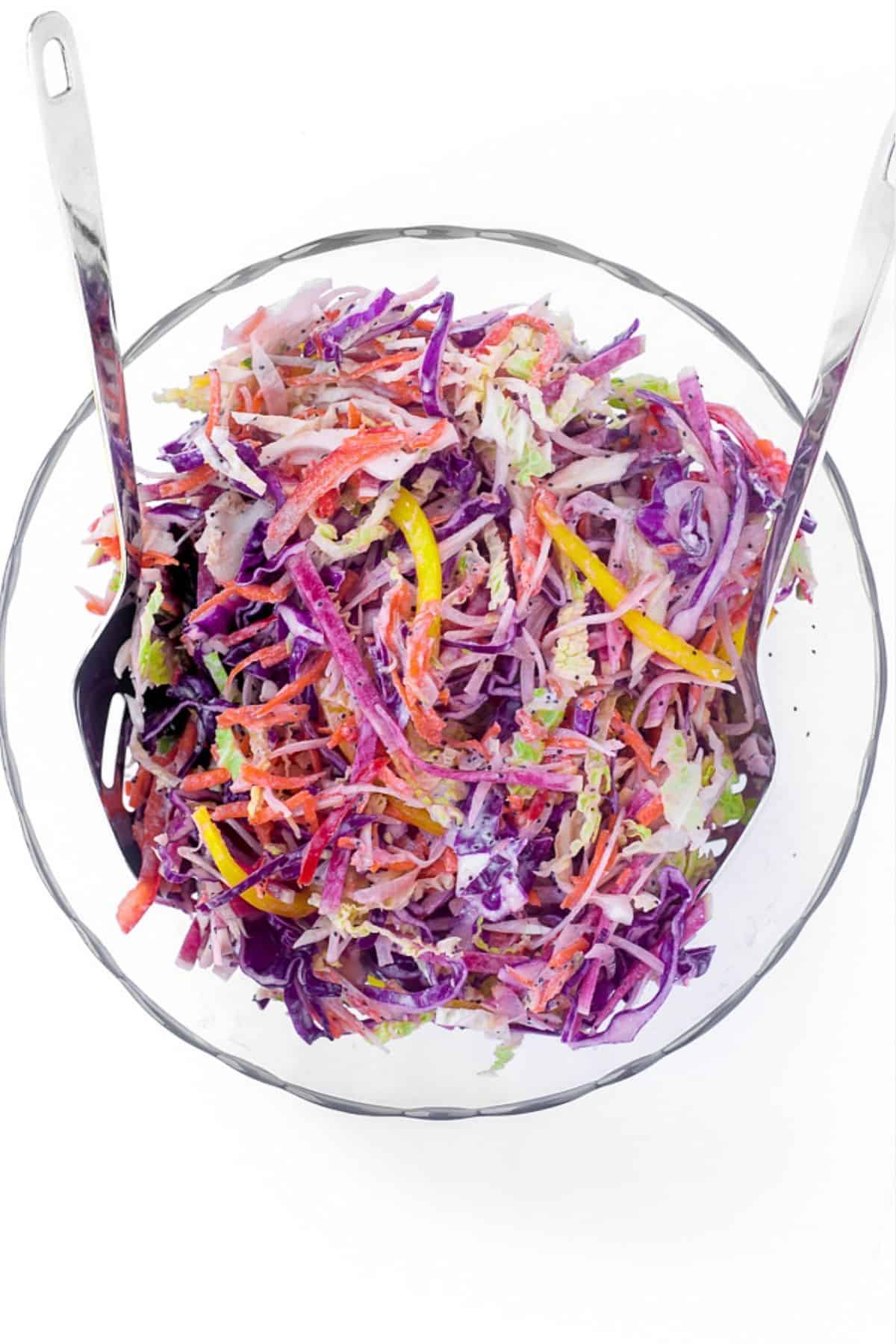 Tossing rainbow slaw in a glass bowl.