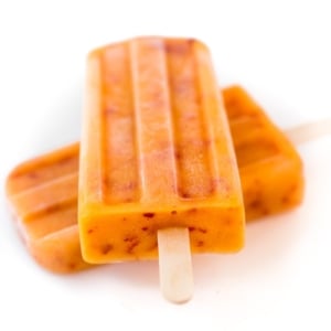 Photo of two ripe peach popsicles laying on a white surface.