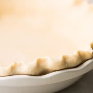 Pie crust, unbaked, in a white ceramic pie dish.