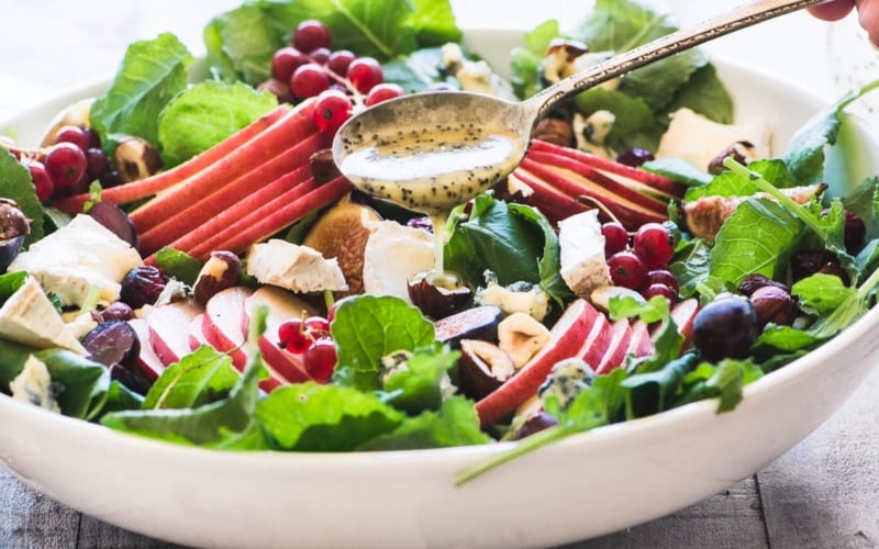Drizzling cider poppy seed dressing on a kale and fall fruit salad