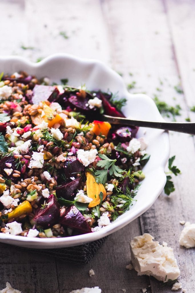 Rye berry and beet salad in a white bowl with serving spoon