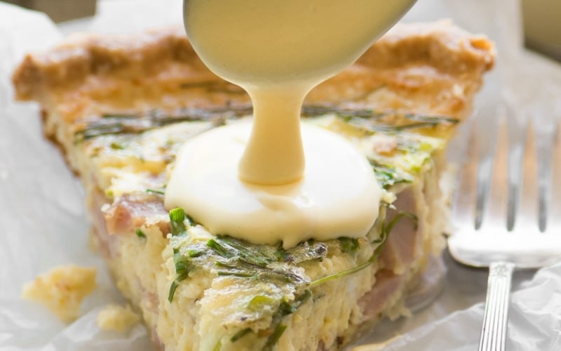 spooning hollandaise sauce on quiche