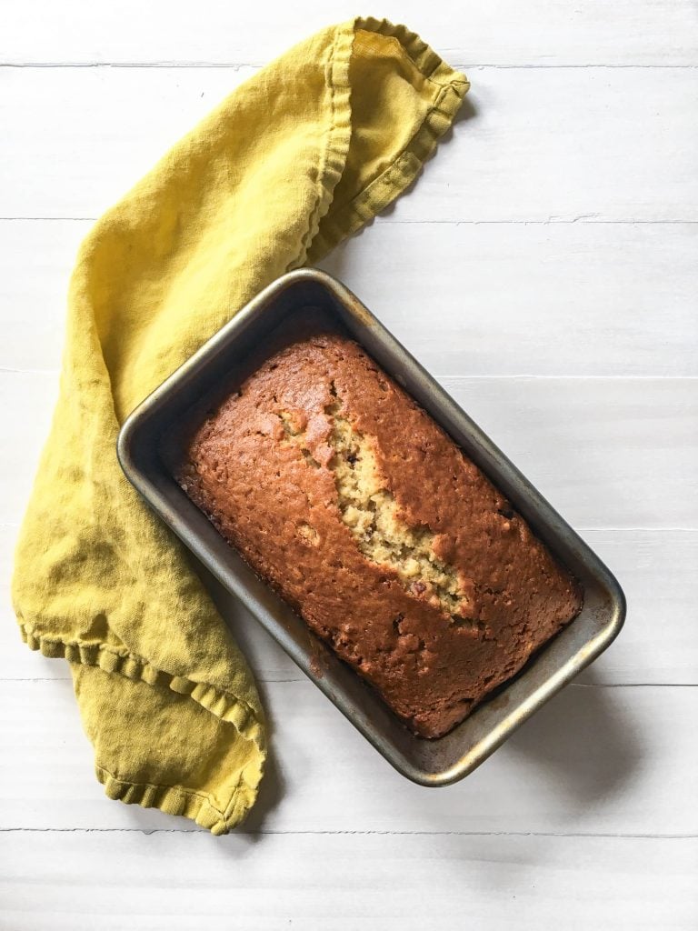 one banana banana bread in loaf pan with yellow napkin
