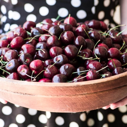 girl holding large wooden bowl of cherries