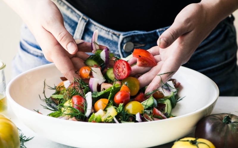 Hands tossing a Shirazi Salad in a white bowl