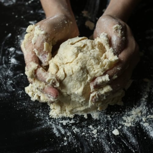 hands making pie dough on a dark ground