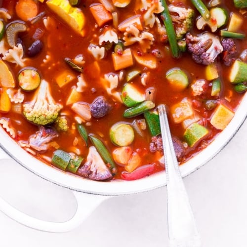 Minestrone soup in a white cast iron soup pot with ladle