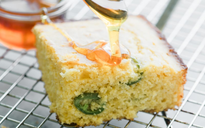 drizzling honey on a piece of honey jalapeño cornbread