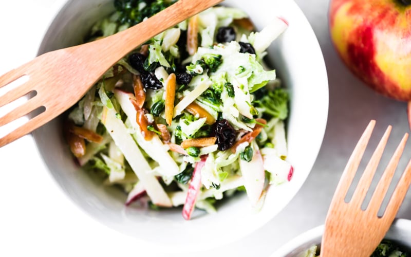 Broccoli Honeycrisp Slaw in a small white bowl with a bamboo fork