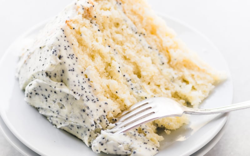A slice of lemon cake with lemon poppy seed buttercream on a small plate with fork