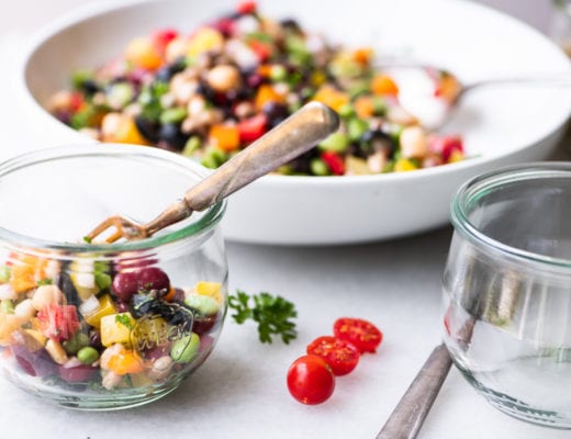 spponing rainbow bean salad into glass bowls