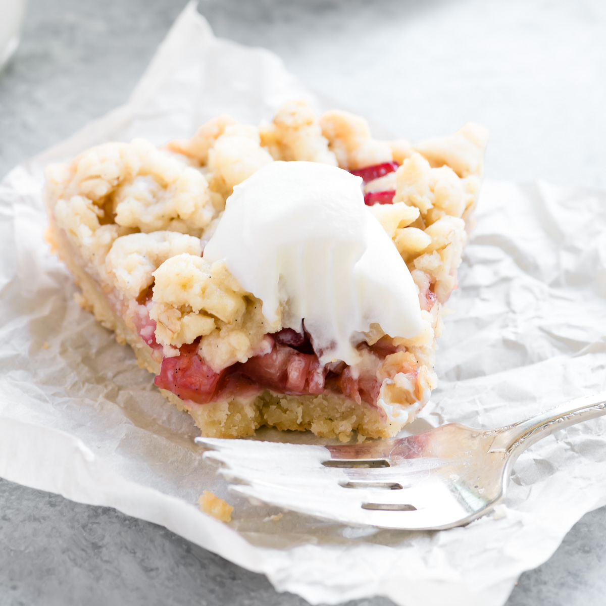 a slice of rhubarb shortbread crumble tart with whipped cream