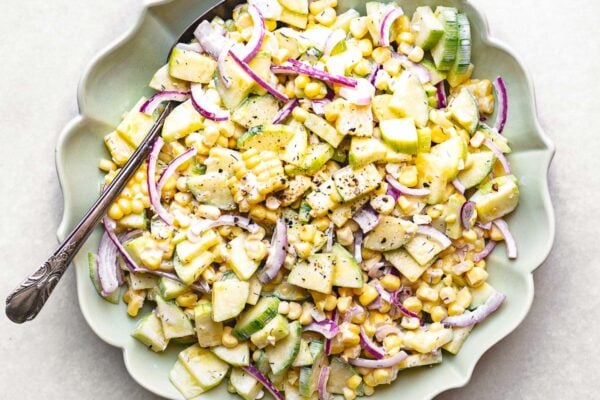 corn and cucumber salad in a bowl with serving spoon.