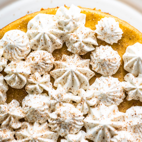 pumpkin spice cheesecake topped with piped whipped cream and nutmeg