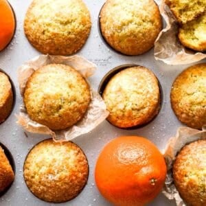orange cardamom muffins in a muffin tin with fresh oranges.