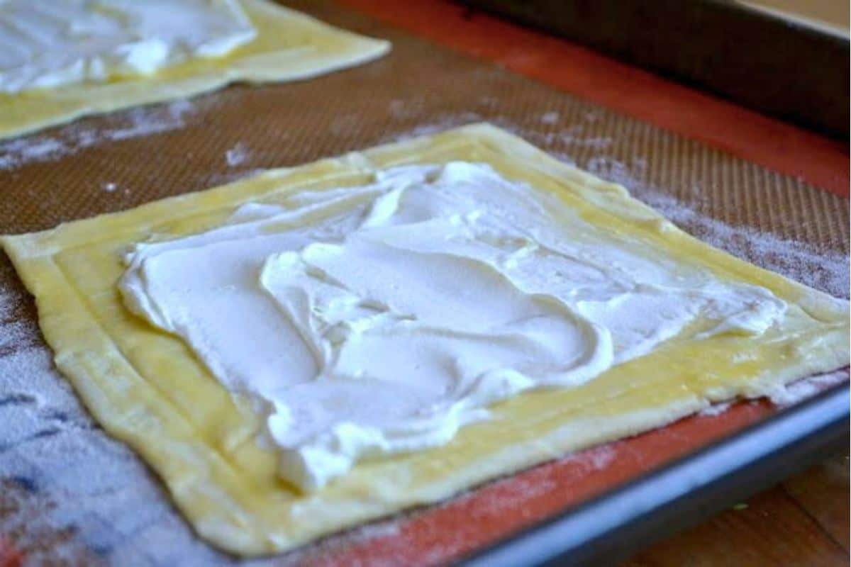 Red Pepper and Baked Egg Galettes from Jerusalem (the book) ~ these eggs baked in puff pastry are the ultimate breakfast in bed recipe! #eggs #breakfast #brunch #puffpastry #bakedeggs #breakfastinbed #mothersday #valentinesday #Christmasbreakfast #holidaybreakfast #ottolenghi #jerusalem cheese spread on puff pastry for egg galettes.