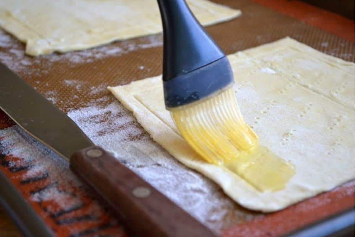 Red Pepper and Baked Egg Galettes from Jerusalem (the book) ~ these eggs baked in puff pastry are the ultimate breakfast in bed recipe! #eggs #breakfast #brunch #puffpastry #bakedeggs #breakfastinbed #mothersday #valentinesday #Christmasbreakfast #holidaybreakfast #ottolenghi #jerusalem brushing puff pastry for egg galettes.