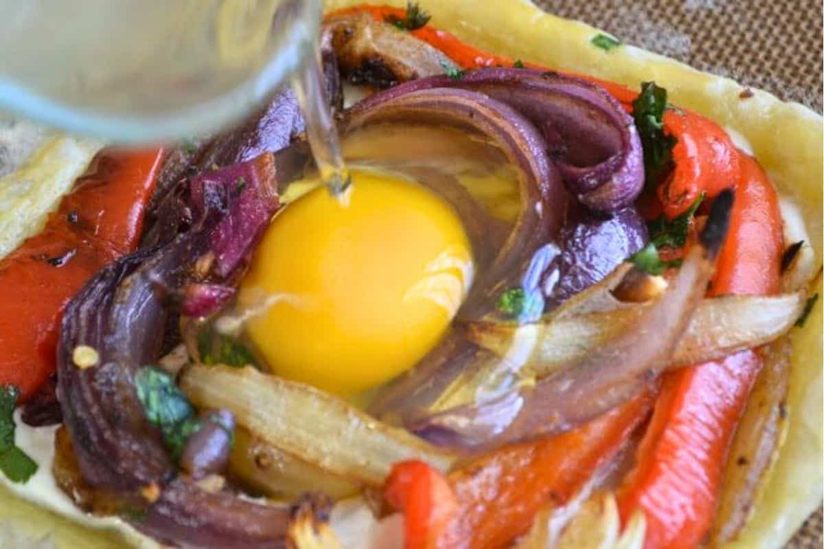 Red Pepper and Baked Egg Galettes from Jerusalem (the book) ~ these eggs baked in puff pastry are the ultimate breakfast in bed recipe! #eggs #breakfast #brunch #puffpastry #bakedeggs #breakfastinbed #mothersday #valentinesday #Christmasbreakfast #holidaybreakfast #ottolenghi #jerusalem gently adding egg to egg galette.