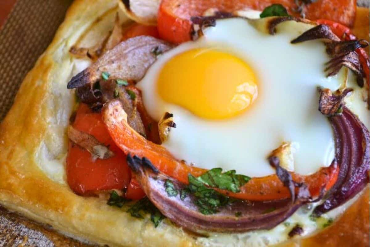 Red Pepper and Baked Egg Galettes from Jerusalem (the book) ~ these eggs baked in puff pastry are the ultimate breakfast in bed recipe! #eggs #breakfast #brunch #puffpastry #bakedeggs #breakfastinbed #mothersday #valentinesday #Christmasbreakfast #holidaybreakfast #ottolenghi #jerusalem Ottolenghi's red pepper and egg galettes on a baking sheet.