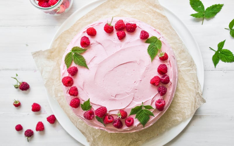 Raspberry layer cake topped with raspberries and raspberry leaves.