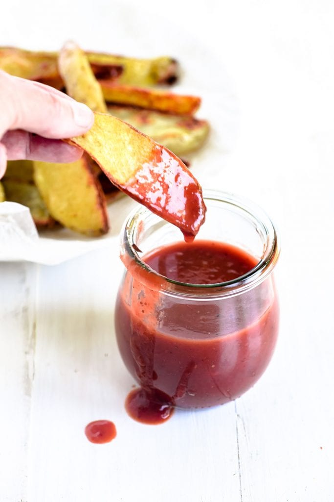 Dipping oven fries into a pot of strawberry barbecue sauce