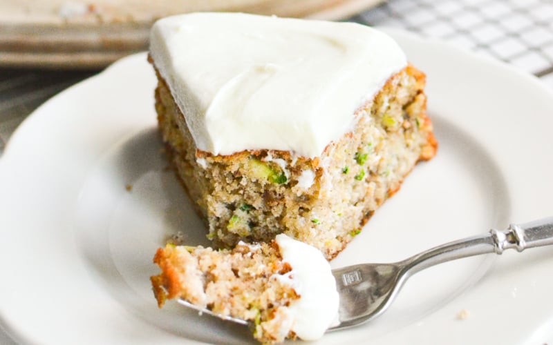 A slice of zucchini cake on a plate with a fork taking a bite.