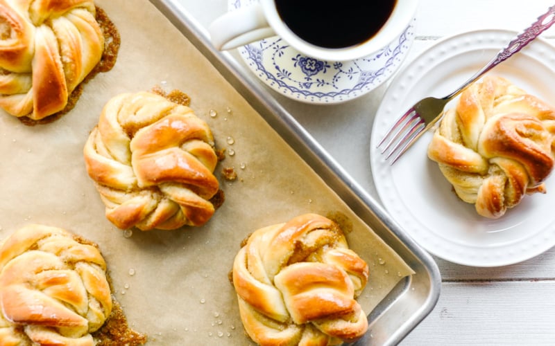 cardamom buns on a baking tray with cup of coffee