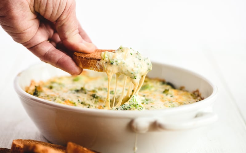scooping up broccoli cheese dip with a piece of toast