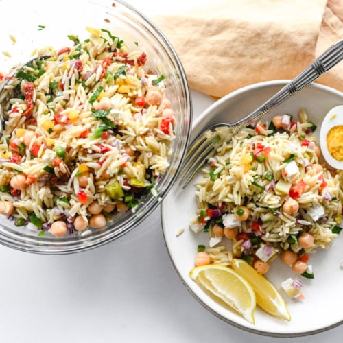 A bowl of orzo salad with plate, napkin, and fork