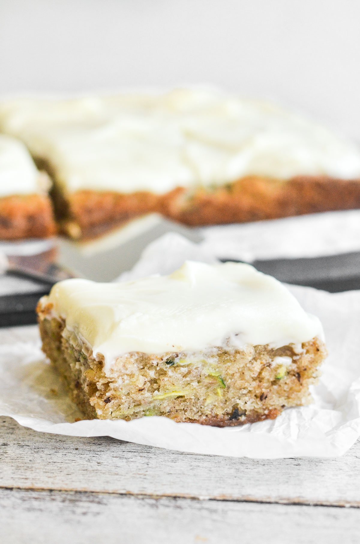 A slice of zucchini sheet cake on a piece of parchment paper.