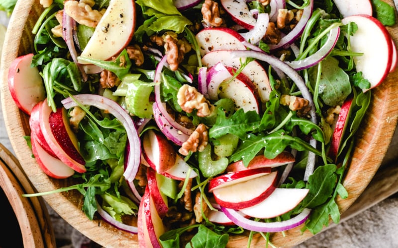 apple celery and walnut salad in a wooden bowl with salad servers