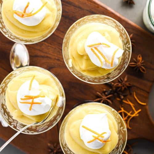 Four glasses of winter spice vanilla pudding topped with whipped cream and orange peel.