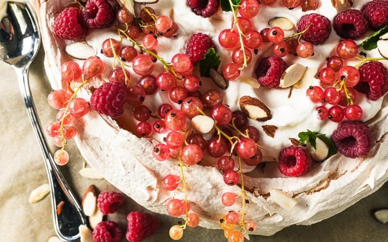 a soft almond pavlova topped with whipped cream and currants